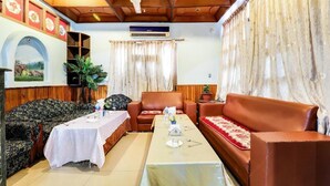 A room with a long table set for dining, two sofas, a ceiling fan, and a wall-mounted air conditioner.