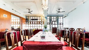 A dining hall with long tables, red upholstered chairs, chandeliers, and ceiling fans.