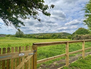 A wooden gate with a sign, a grassy field, and hills in the background.