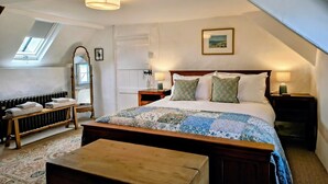 Une chambre à coucher avec un grand lit, un banc en bois, un radiateur, un miroir et une lucarne.