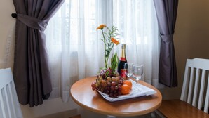 A round wooden table with a centerpiece of grapes, an orange, and a flower arrangement. A bottle and two glasses are also on the table. - Senses Central Hotel (Ho Chi Minh City)