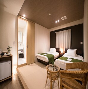 Ein Hotelzimmer mit zwei Betten, einem kleinen Schreibtisch, einem Korbstuhl und einem Glastisch.