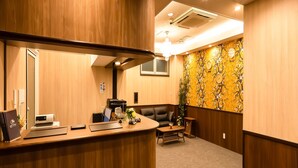 A hotel reception area with a wooden reception desk, a black leather sofa, and a decorative wall with a floral pattern. - Hotel Cozy Taito Asakusa (Tokyo)
