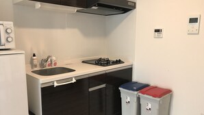 Eine kompakte Küche mit Mikrowelle, Backofen, Gasherd und Spüle. Es gibt zwei Mülleimer und einen kleinen Kühlschrank.