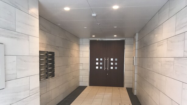 Ein Flur mit Fliesenboden, einer dunklen Tür mit Kartenleser und einem an der Wand montierten Schlüsselausgabegerät.
