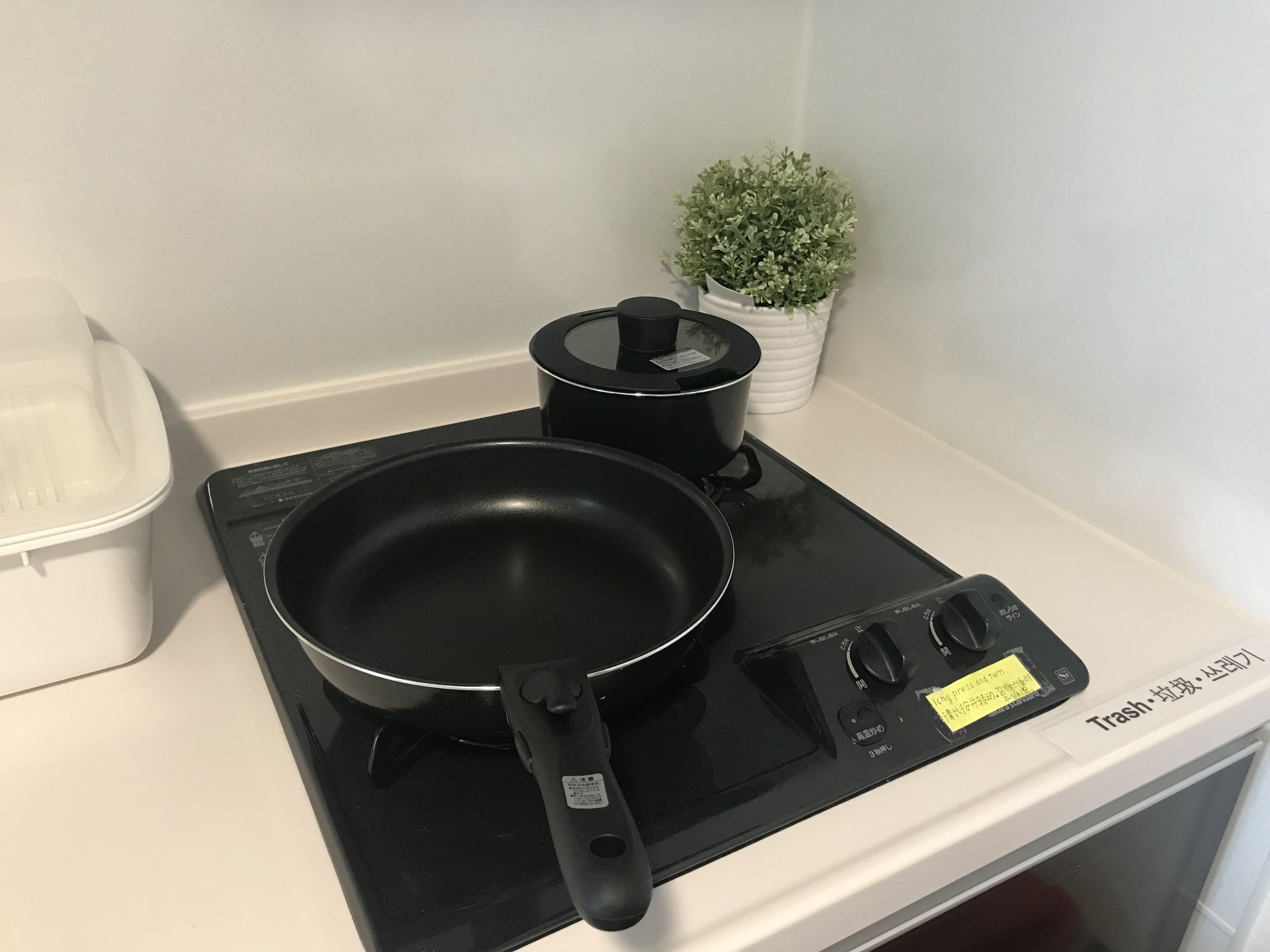 Een keuken met een zwart inductiekookveld, een koekenpan, een pan en een afvalbak.