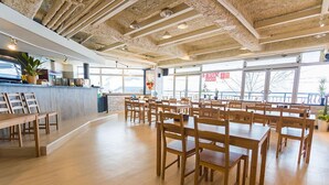 A spacious restaurant with wooden tables and chairs, a counter with a plant, and large windows offering a view. - Hakuba Gateway Hotel (Hakuba)