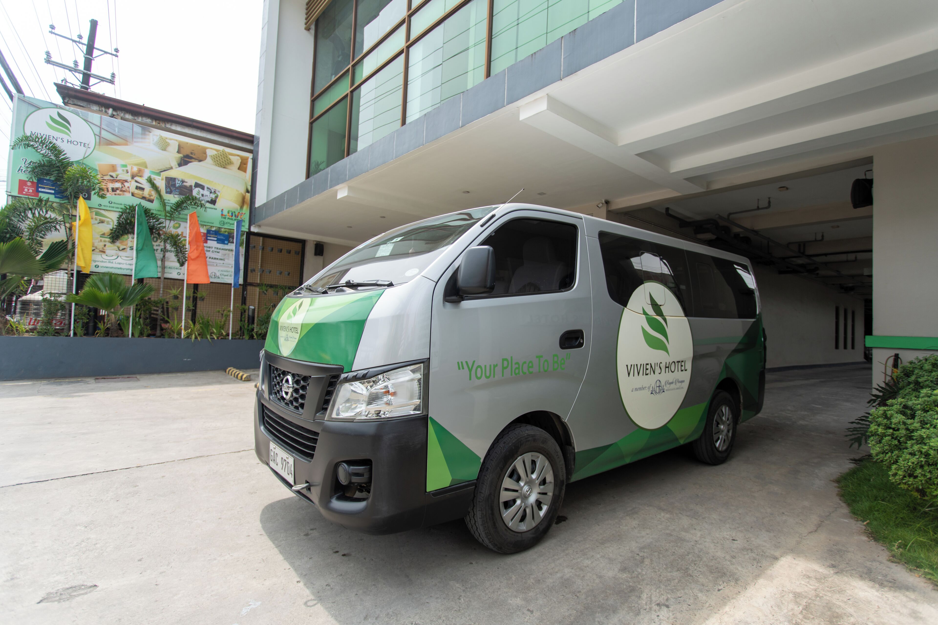 Una camioneta verde y blanca estacionada frente a un edificio con un letrero que dice 'VIVIEN'S HOTEL'.