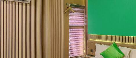 Habitación de hotel con cama, ventana con persianas, aire acondicionado de pared y una pared de acento verde.