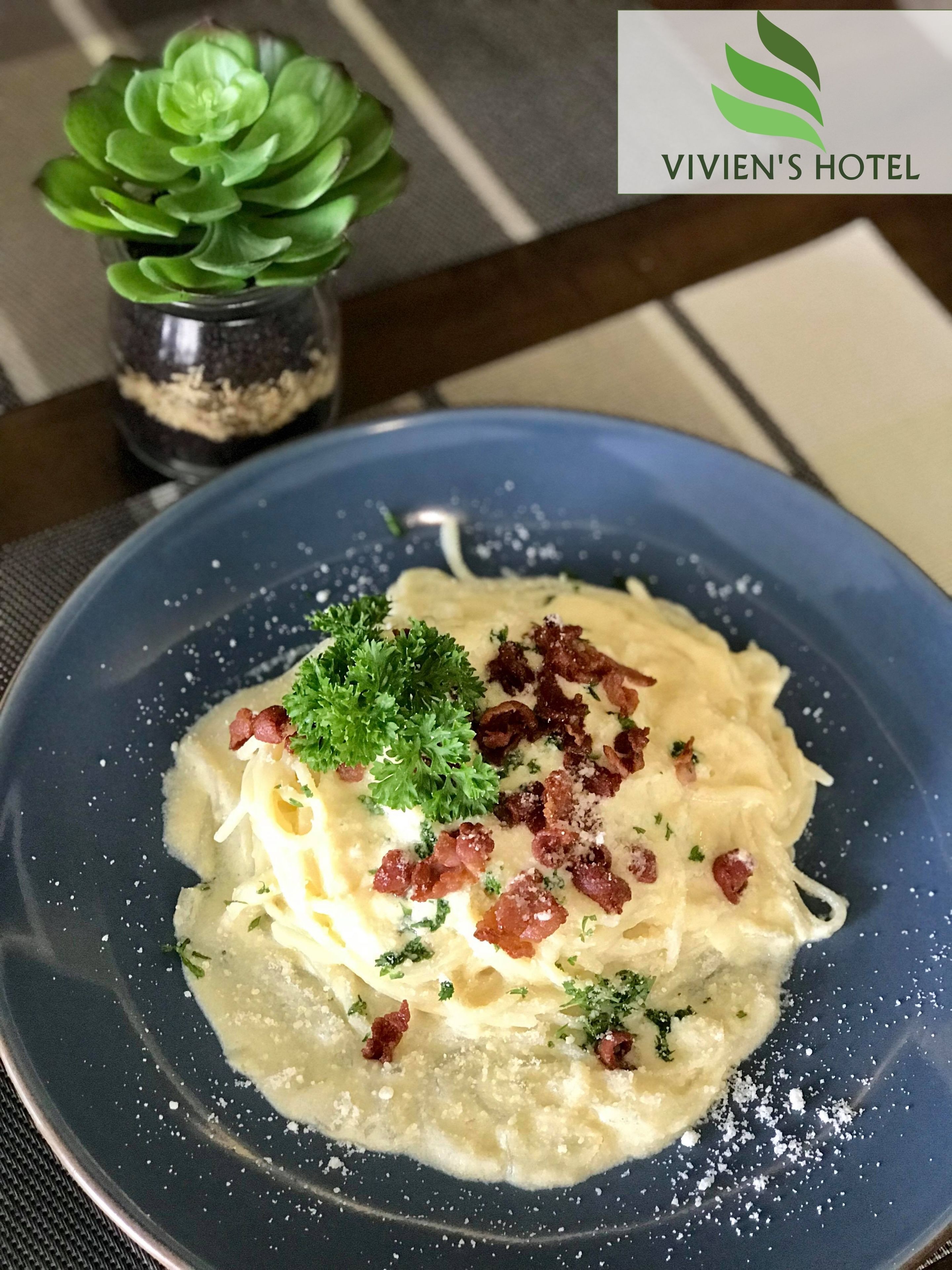 A plate of pasta with bacon and parsley garnish on a blue plate.