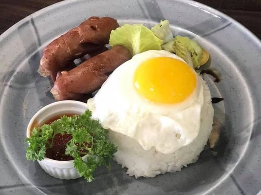 Een bord met gebakken ei over rijst, worst, sla en een klein schaaltje saus.