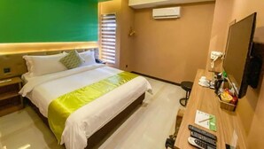 Habitación de hotel con cama, escritorio, silla, televisor y aire acondicionado.
