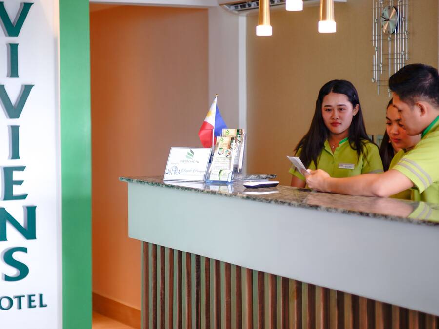 A reception desk at VIVENS HOTEL with a flag, a sign, and two staff members.