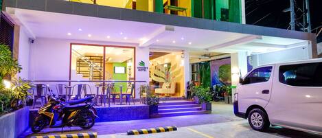 A hotel entrance with a staircase leading to the lobby, a parked motorcycle, and a white van.