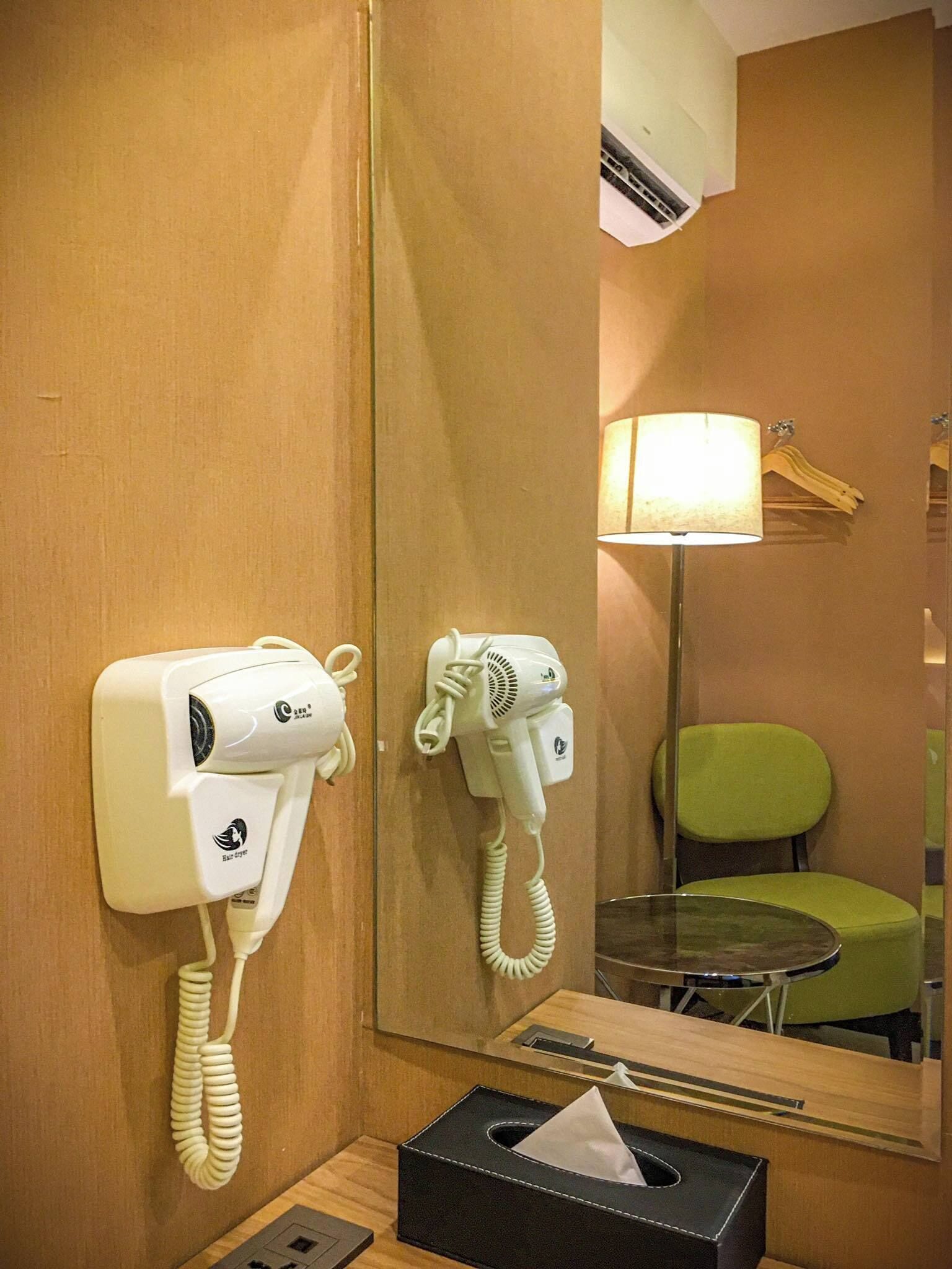 Habitación de hotel con secador y teléfono en la pared, una silla verde, una mesa y una caja de pañuelos.