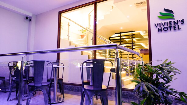 Un vestíbulo de hotel con entrada de vidrio, una escalera y un área de descanso con sillas y mesas.