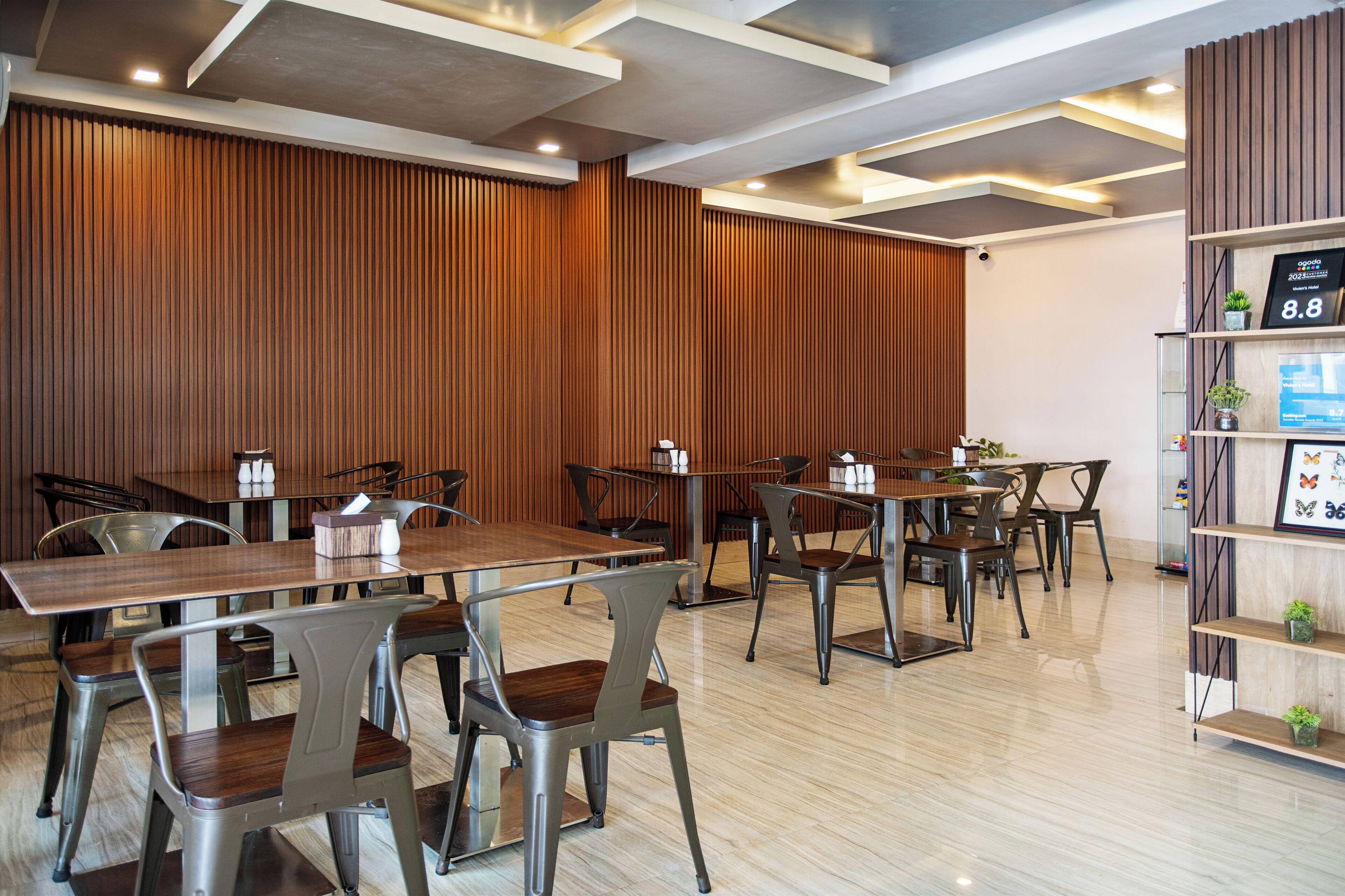 A modern hotel room with wooden panel walls, a wooden floor, and a reception desk with a digital display.