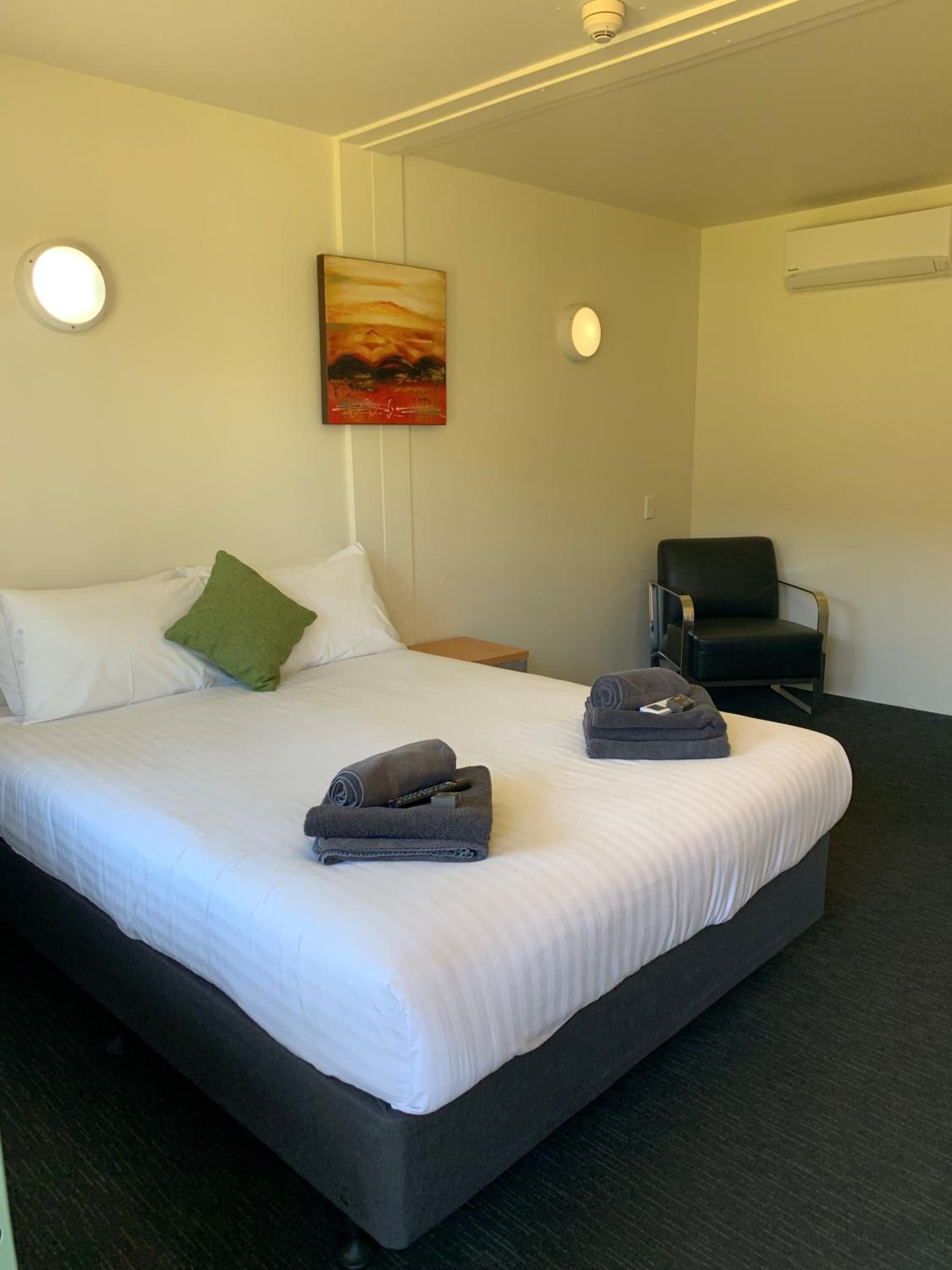 Ein Hotelzimmer mit einem großen Bett, einem Sessel, einem Bild an der Wand und einer Klimaanlage.