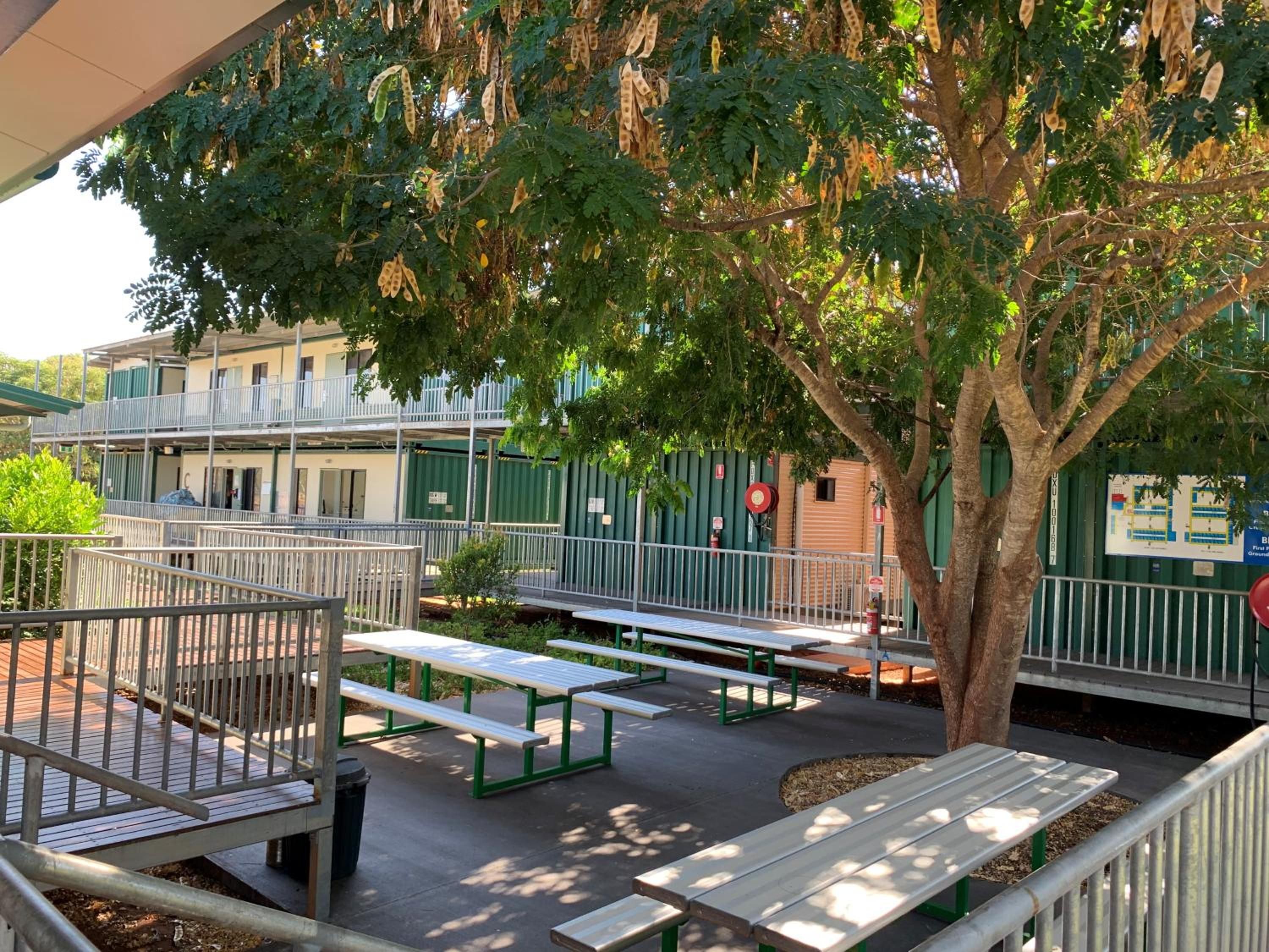 Zona de estar al aire libre con mesas de picnic y un árbol que da sombra.