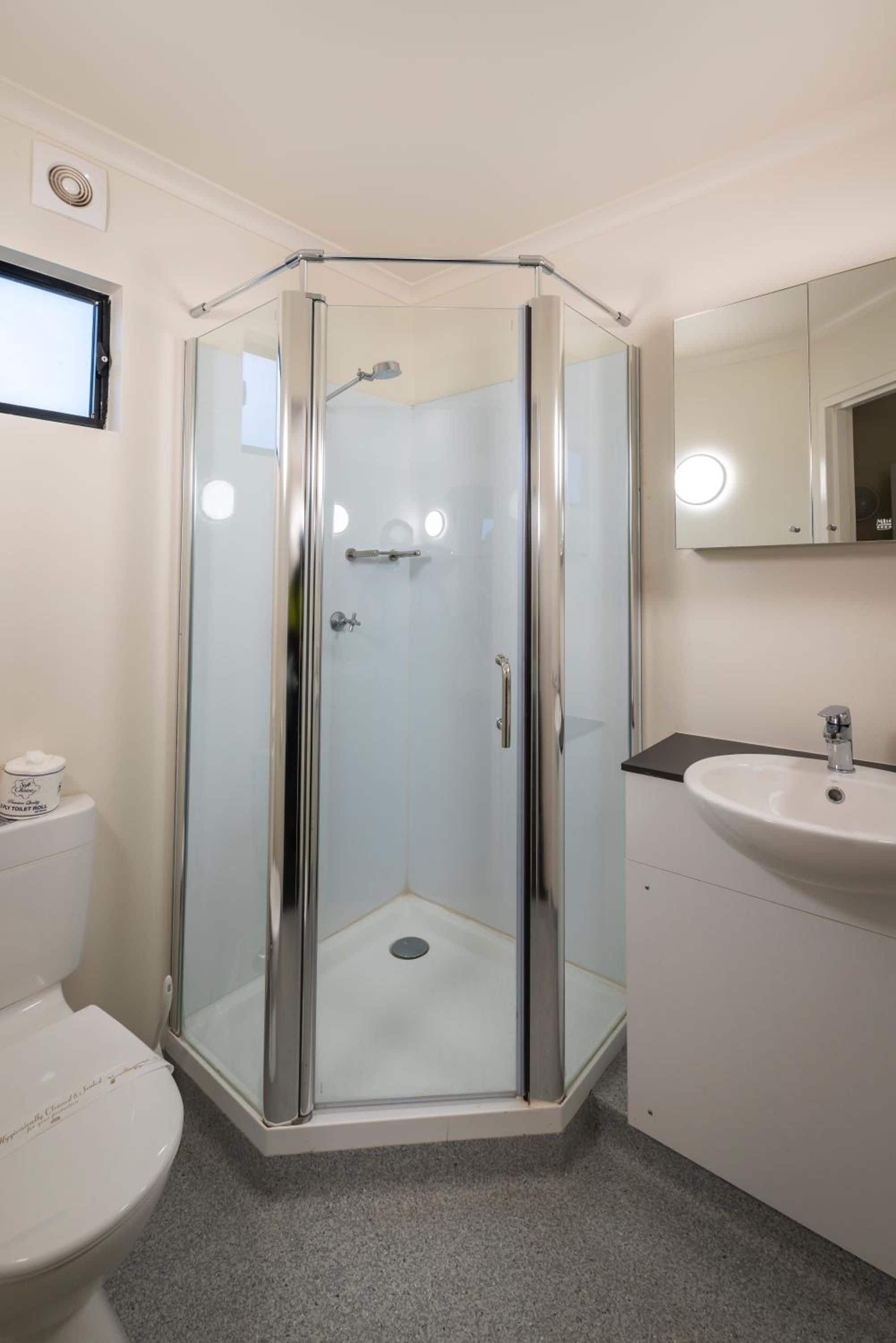 A modern bathroom with a glass-enclosed shower, a toilet, and a sink with a mirror above it.