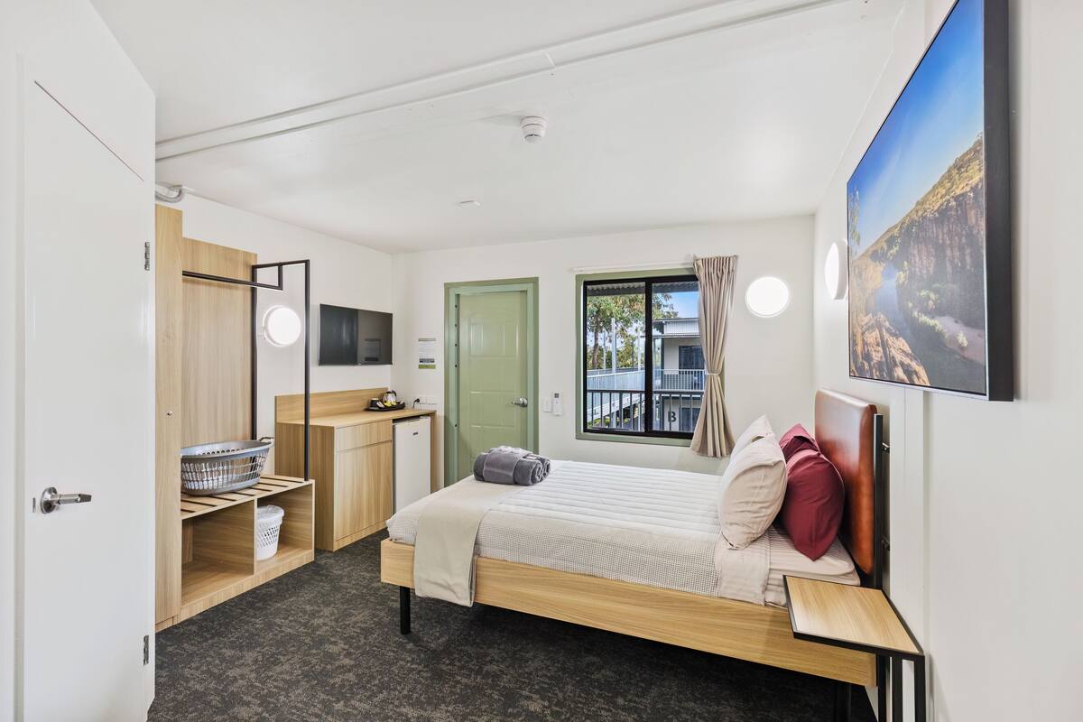 A modern bedroom with a bed, a desk, a wardrobe, and a window with a view.