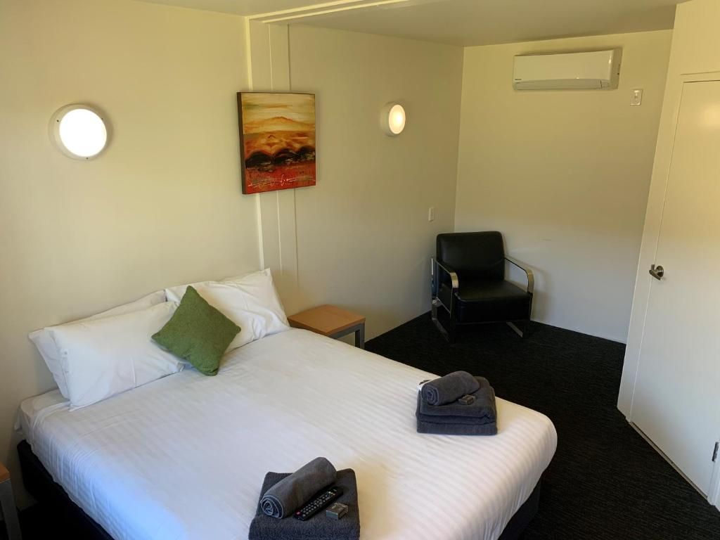 Una habitación de hotel con una cama, una silla, un cuadro en la pared y una puerta.