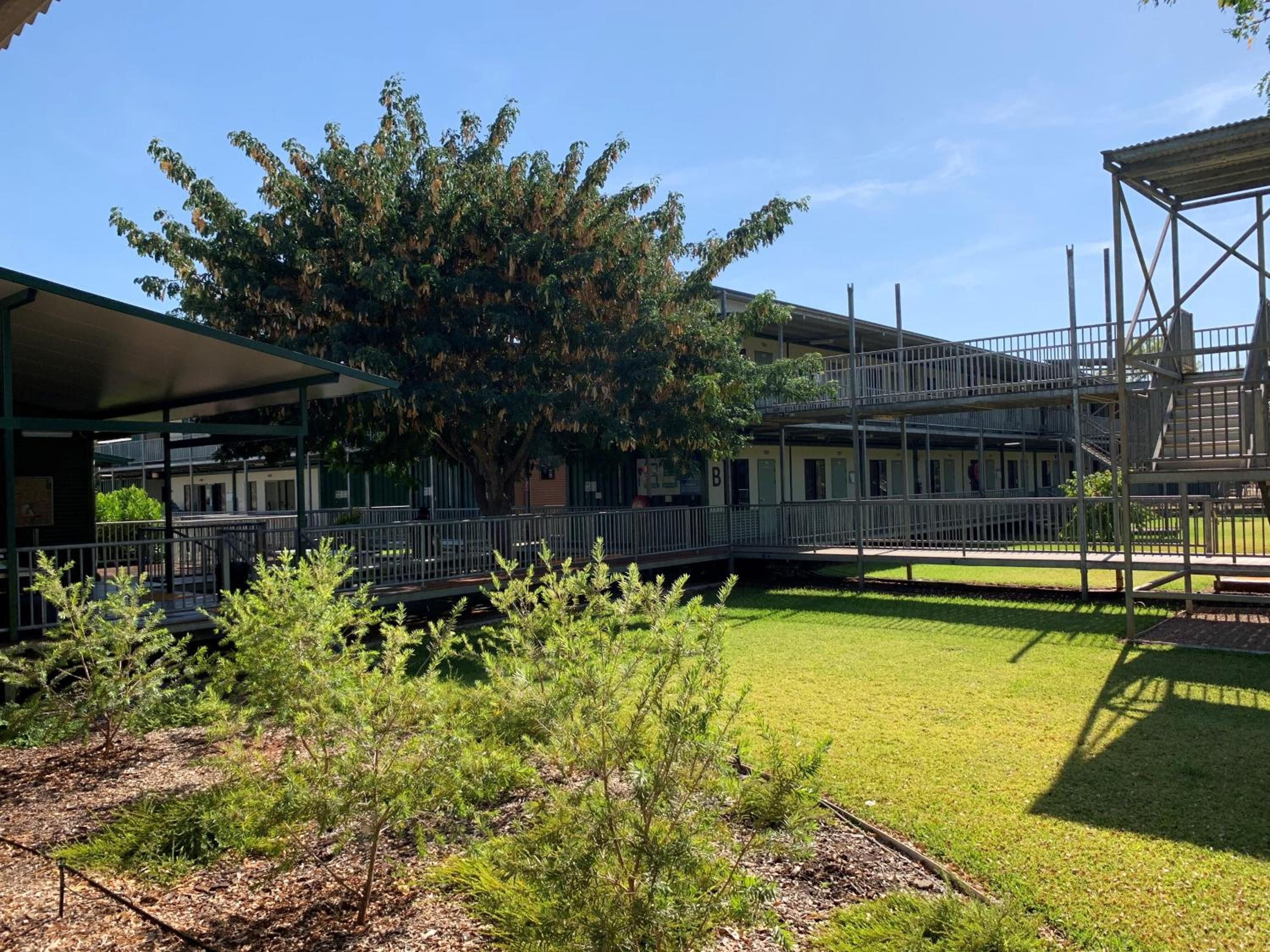 A building with a covered outdoor area, a tree, and a grassy lawn.