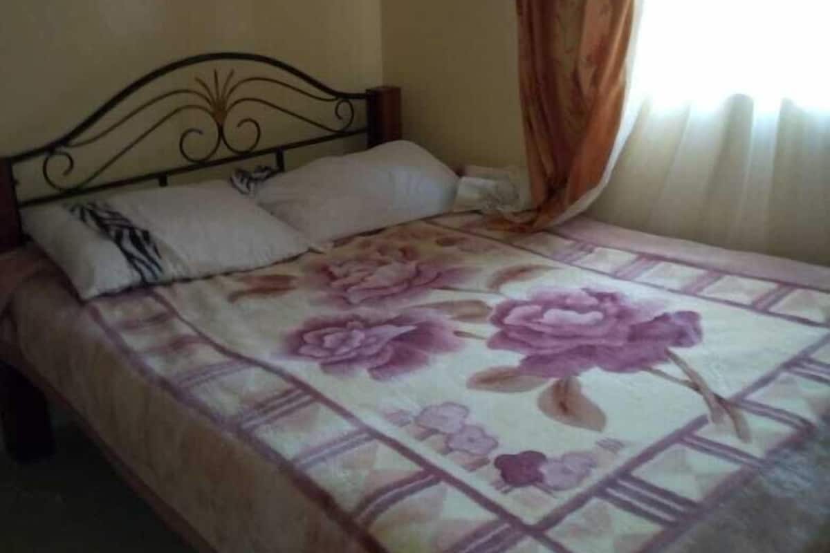 Una cama individual con una colcha estampada, un cabecero y una ventana con cortinas.