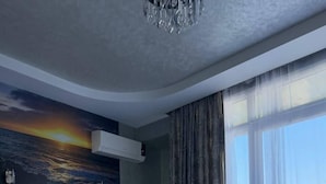 A bedroom with a large bed, a ceiling-mounted air conditioner, a wall mural of a sunset, and a view through sheer curtains. - Black Sea Star Batumi (Batumi)