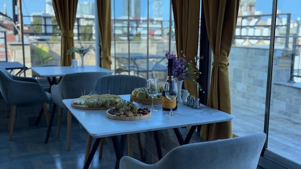 A dining table set with food, wine, and flowers, with a city view through large windows. - Black Sea Star Batumi (Batumi)