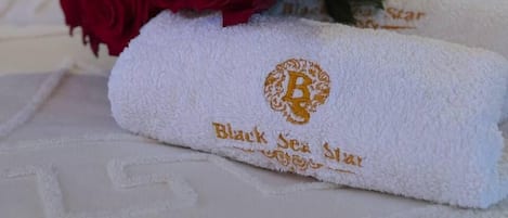 Ein Bett mit weißer Bettwäsche, ein Strauß roter Rosen und Handtücher mit eingesticktem Text.