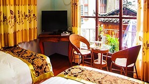 A hotel room with a bed, a desk with a television, a chair, and a table with a plant.