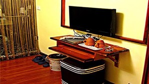 A room with a television mounted on a wall, a wooden desk with a computer and a cup, and a trash bin.