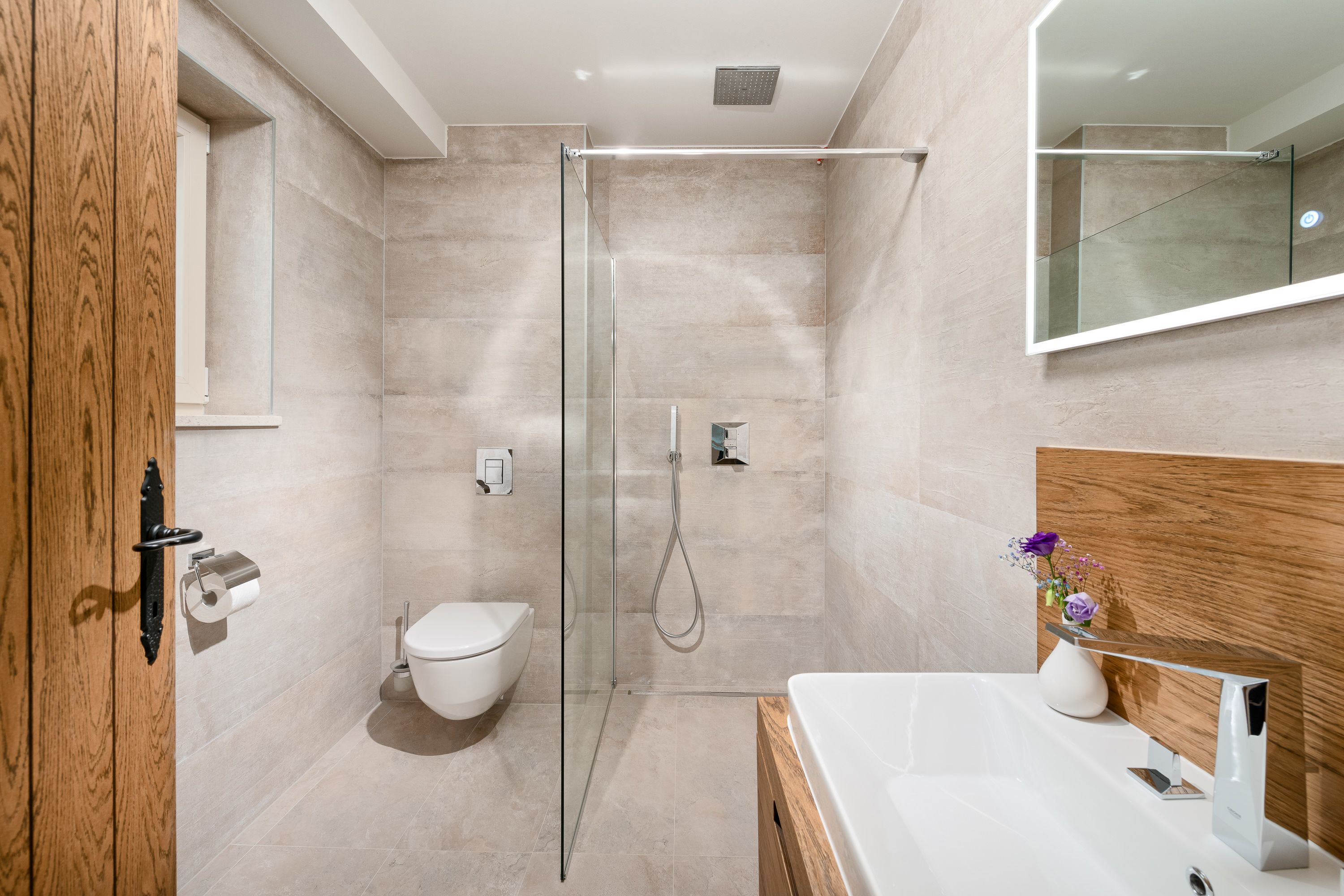 A modern bathroom with a glass shower enclosure, a toilet, and a sink with a wooden vanity.