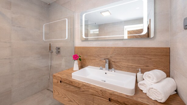 Un baño moderno con tocador de madera, un espejo grande y una ducha.