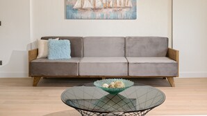 Un salón moderno con un sofá gris, una mesa de centro de vidrio con adornos, y una pintura de veleros en la pared.
