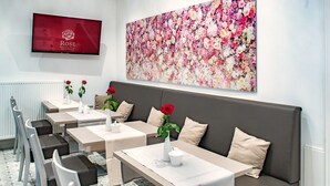 A modern hotel room with a sofa, dining area with tables and chairs, a TV, and a floral artwork on the wall. - Boutique Hotel Rose Baden-Baden (Baden-Baden)
