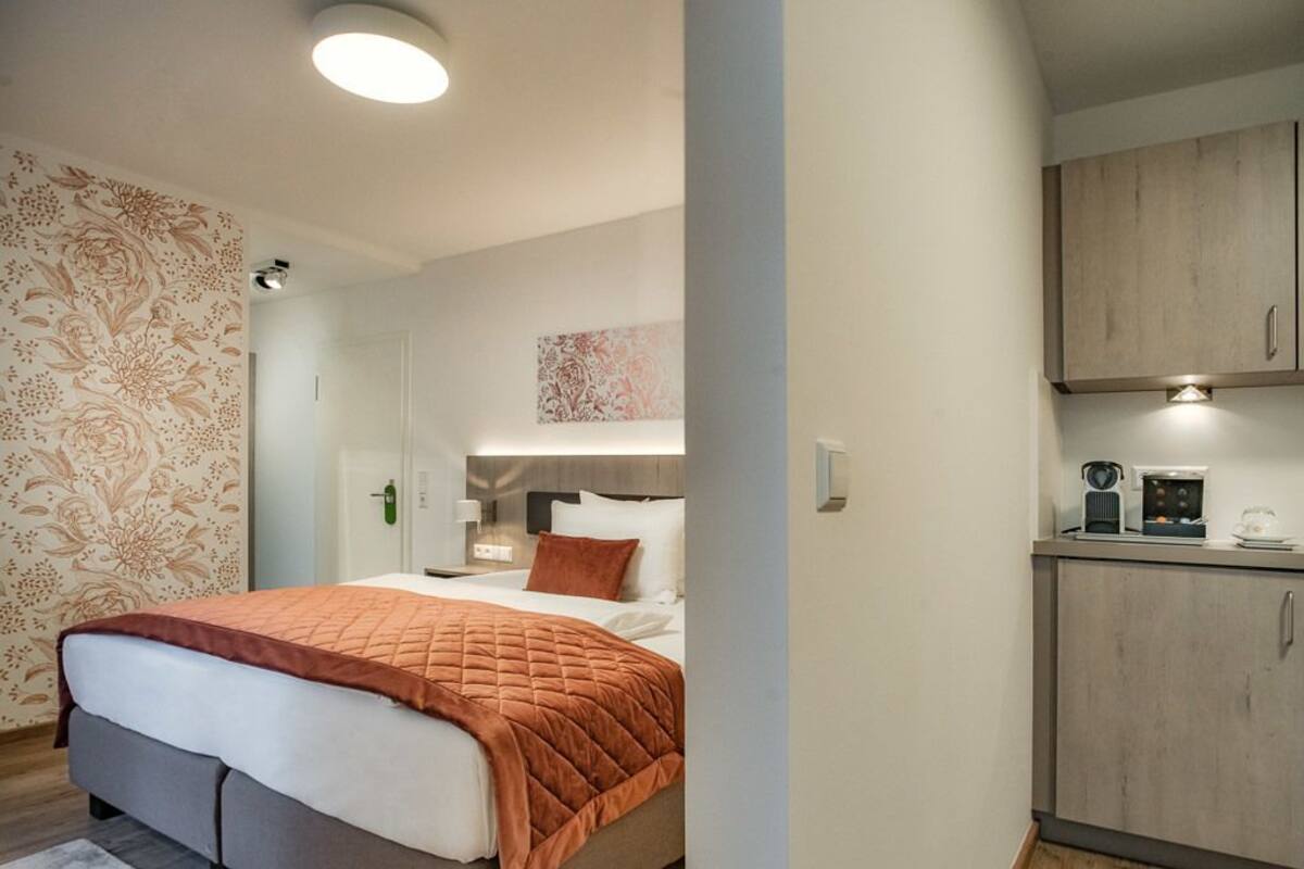 Ein Hotelzimmer mit einem Bett, einem Nachttisch, einer Wandleuchte, einem Schrank und einem Gemälde über dem Bett.