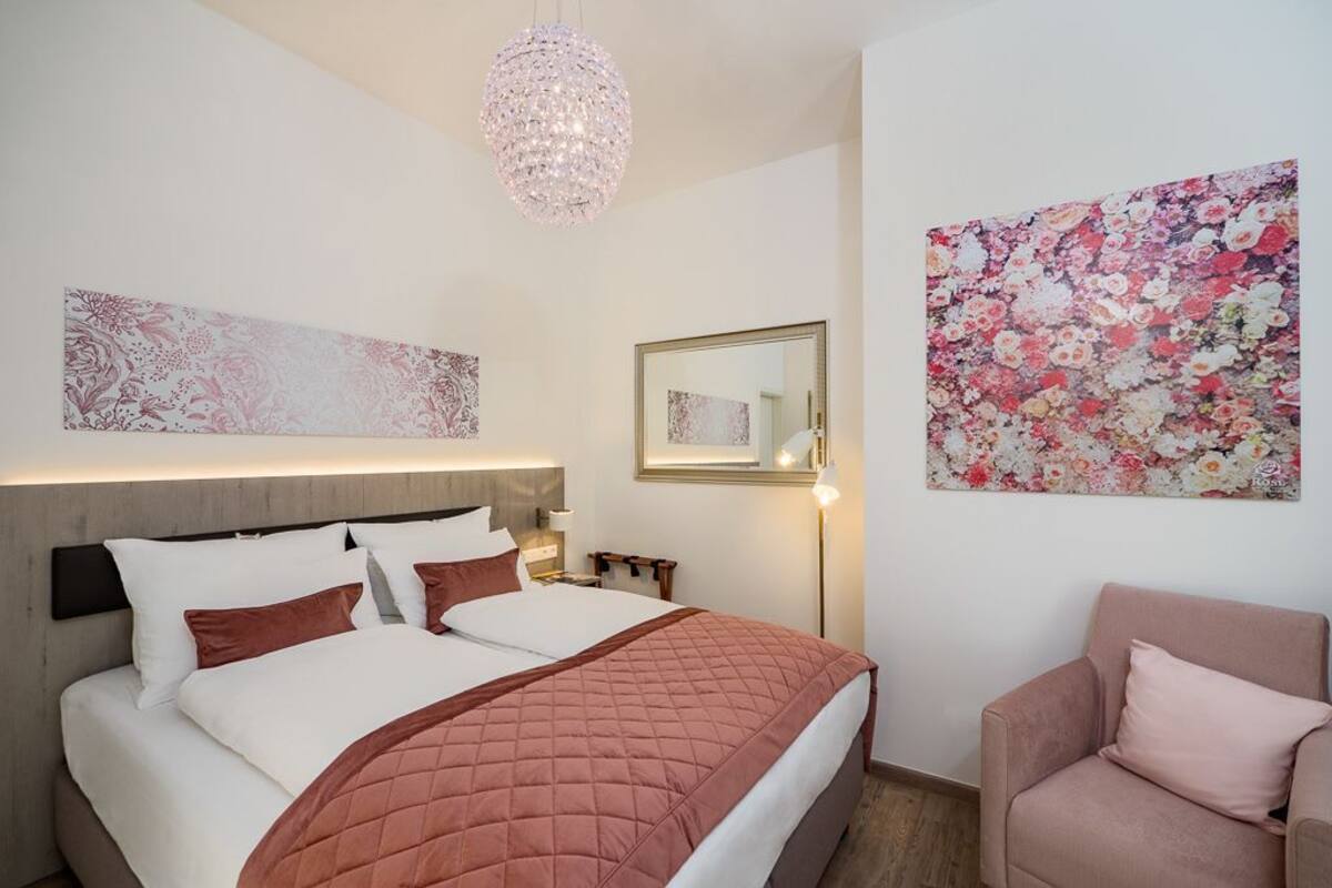 Ein Schlafzimmer mit einem Bett, einem Nachttisch, einem Sessel, einer Pendelleuchte und Wandbildern.