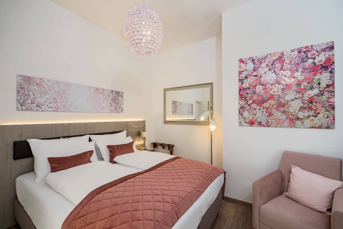 A bedroom with a bed, a bedside table, a chair, a chandelier, and wall art.