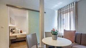 A modern hotel room with a bed, a sofa, a dining table with chairs, and a potted plant. - Boutique Hotel Rose Baden-Baden (Baden-Baden)