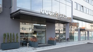 Der Eingang eines Courtyard by Marriott Hotels mit modernem Design, großen Fenstern und Blumentöpfen.