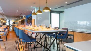 Un comedor moderno con mesas largas, sillas azules e iluminación colgante.