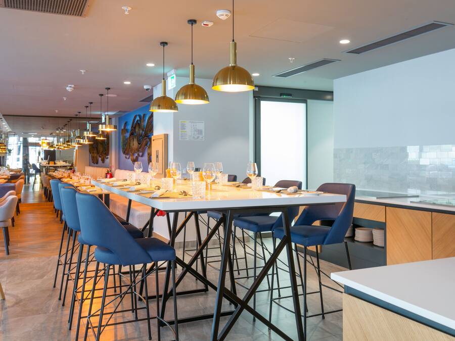 Un comedor moderno con mesas largas, sillas azules e iluminación colgante.