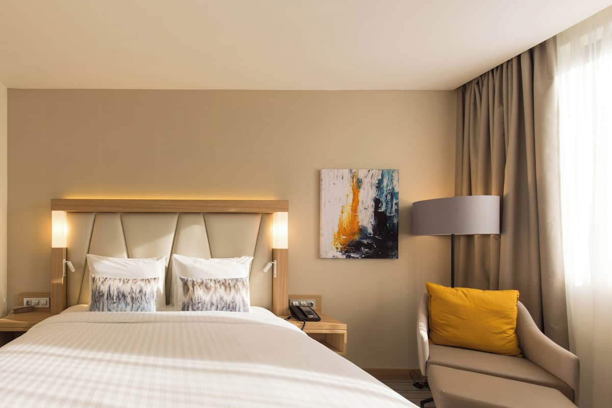 A hotel room with a large bed, two bedside tables, a chair, a lamp, and a painting on the wall.