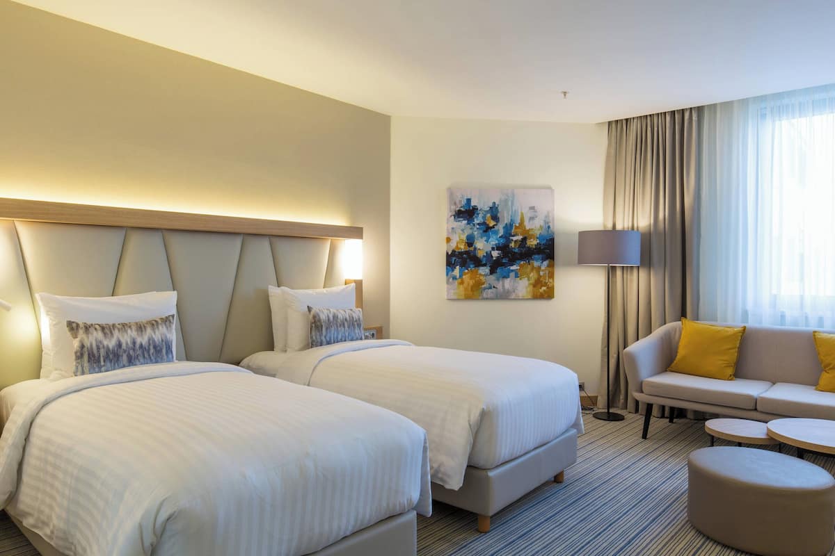 A hotel room with two beds, a sofa, and a small table.