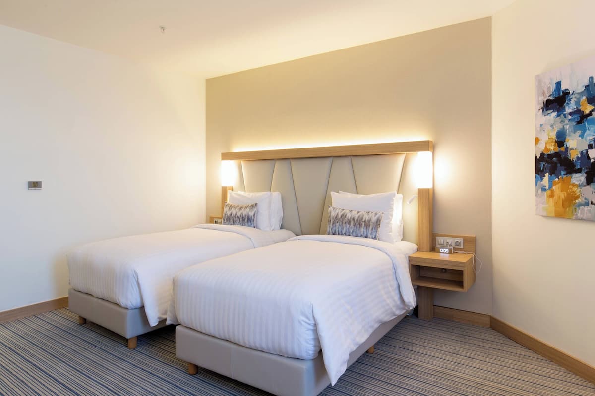 A hotel room with two beds, a nightstand with a lamp, and a painting on the wall.