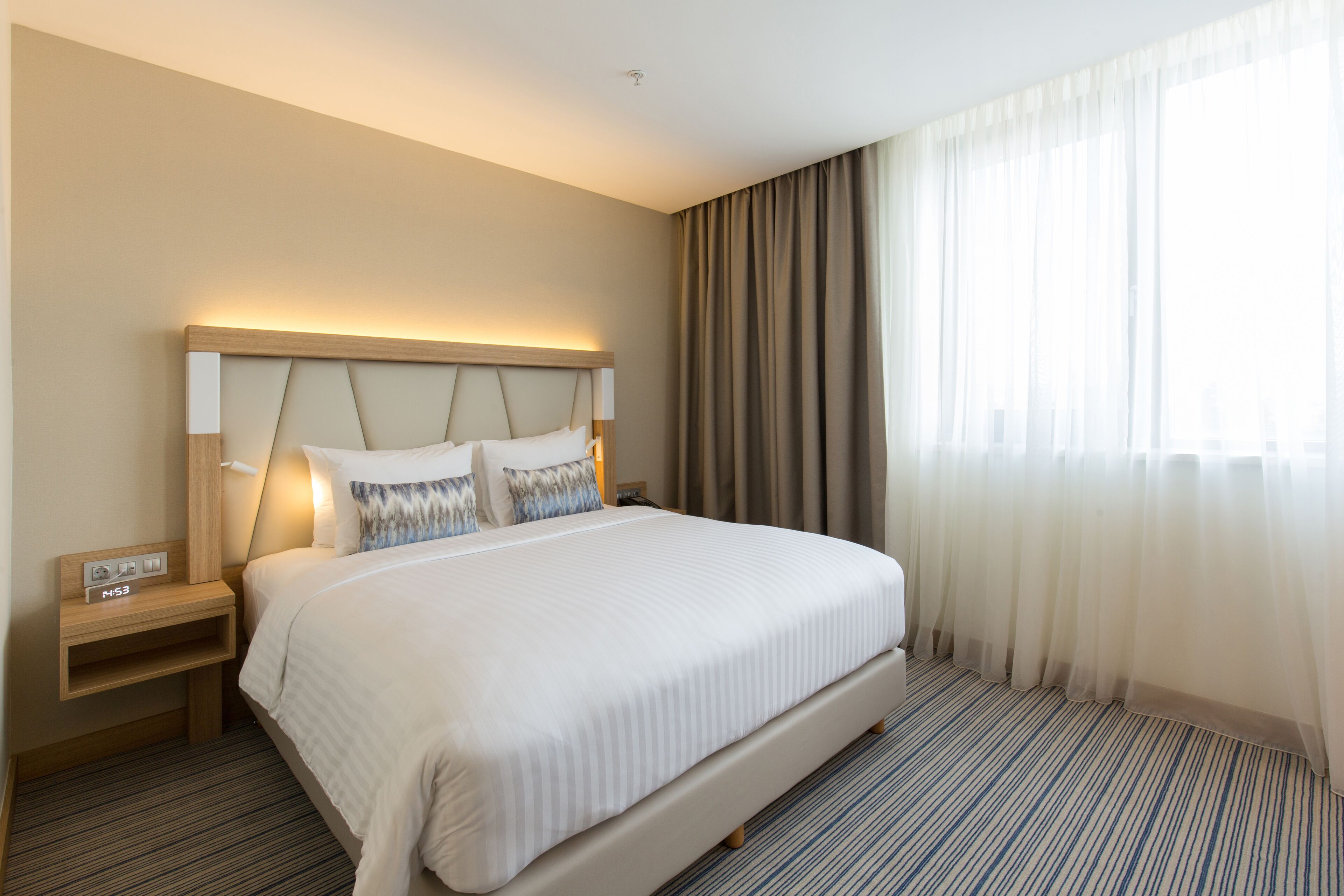 A hotel room with a large bed, a nightstand with a lamp, and a window with curtains.