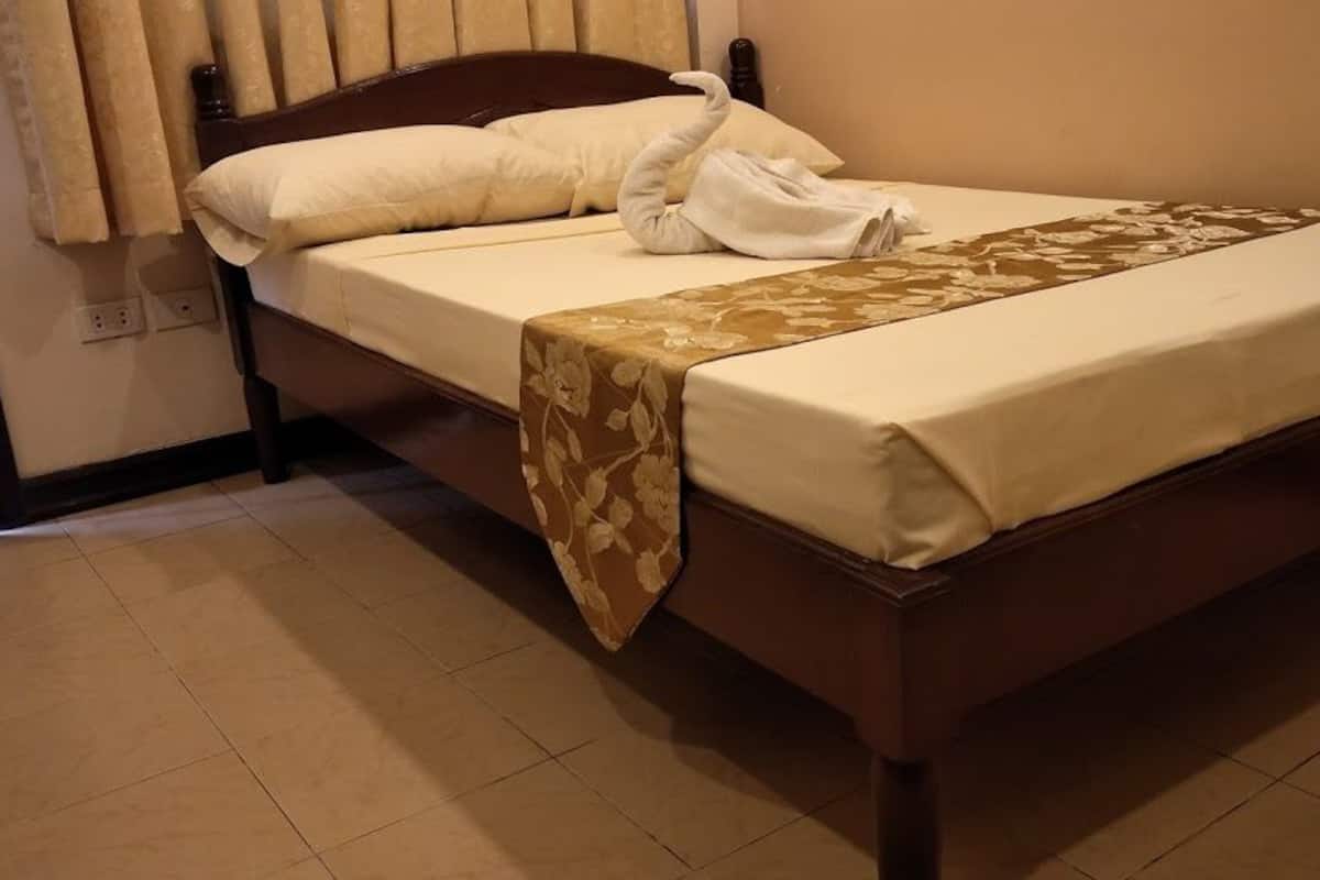 A neatly made bed with a brown headboard, a floral bedspread, and a swan-shaped towel.