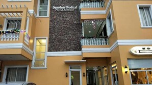 Un edificio con un letrero que indica Dumdum Medical Plaza & Residences. Tiene varios balcones con barandillas, fachada de piedra y una puerta con panel de vidrio.
